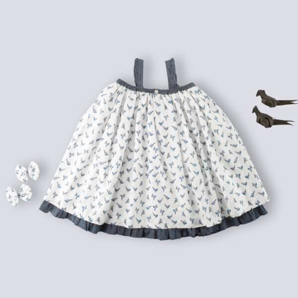 Flatlay of strappy shoulder girls dress with blue bird print and tiny ruffles on the shoulder straps in navy dot fabric