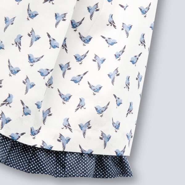 Close-up of hemline in strappy shoulder dress with blue bird print and ruffles on the straps in navy dot fabric