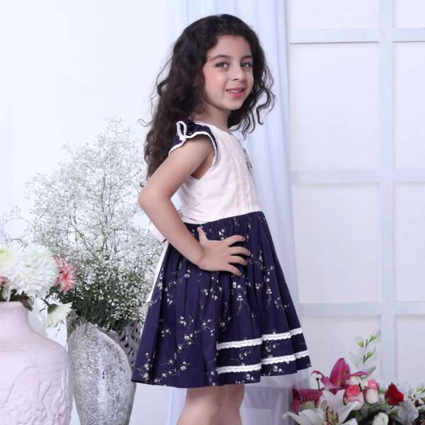 A girl in floral printed cotton navy dress with flutter sleeves, lace trims and hand embroidered bouquet in the yoke