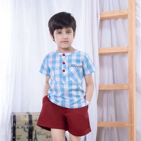 A boy in a striking blue checked shirt with bold red chevron hand-embroidered front pocket and bright red buttons