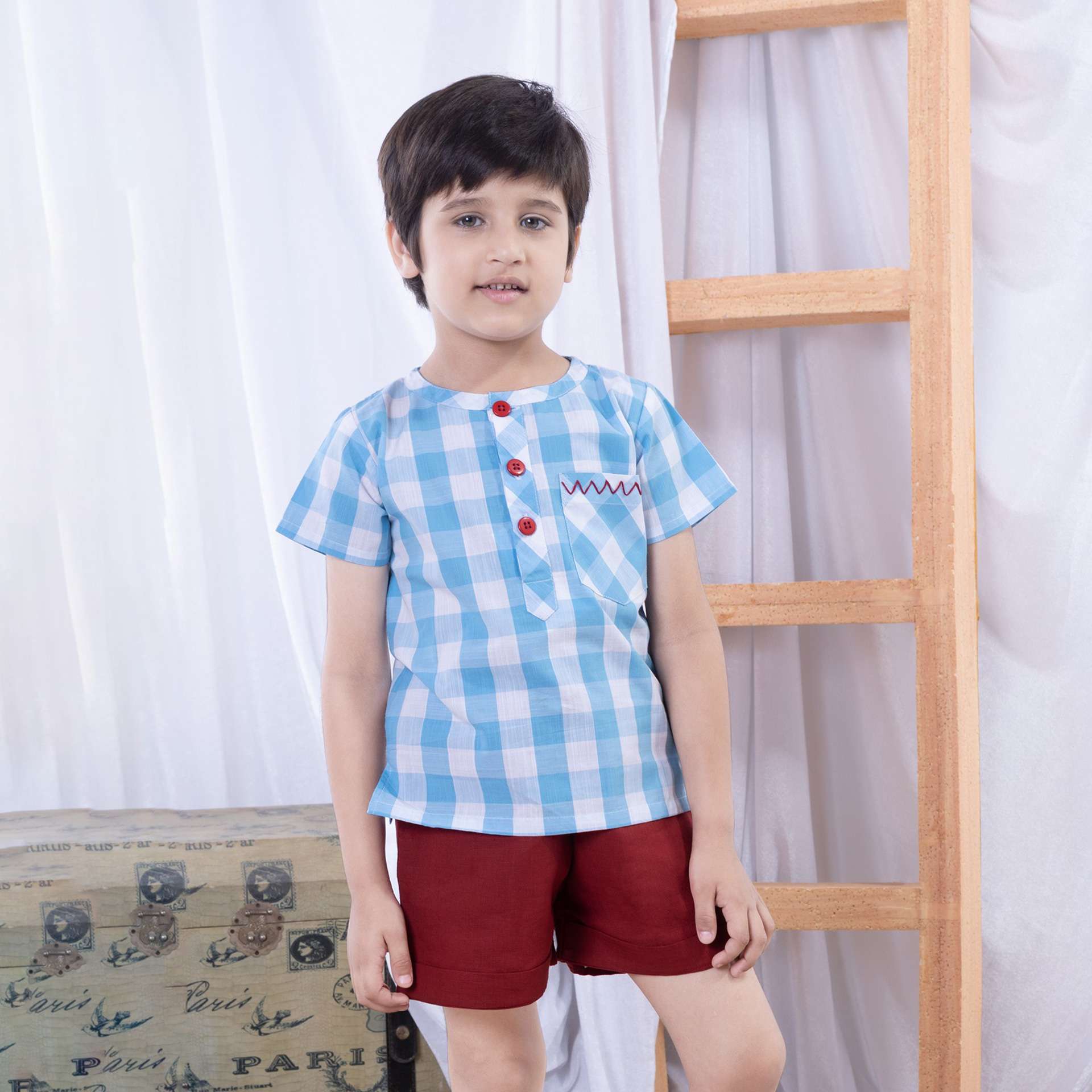 A young boy in blue checked cotton shirt with red chevron hand embroidered front pocket and bright red buttons