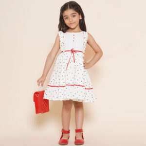 A little girl in sleeveless polka dot ivory cotton dress with red satin belt and hand embroidered bow embellishments