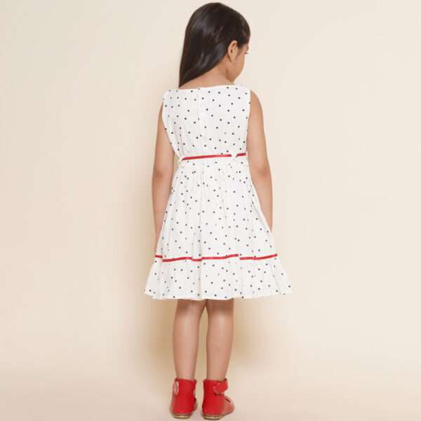 Rear image of girl in sleeveless polka dot ivory cotton dress with red satin belt and hand embroidered bow details