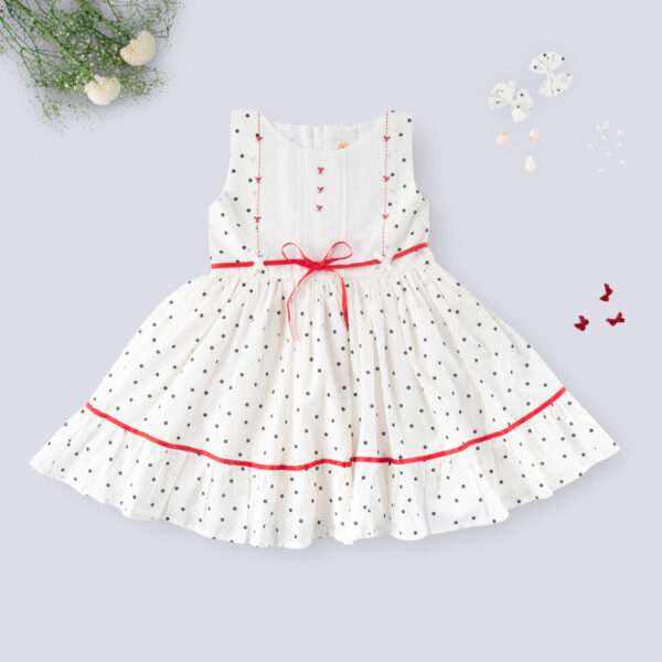 Flatlay of sleeveless polka dot ivory cotton dress with red satin belt and hand embroidered bow embellishments