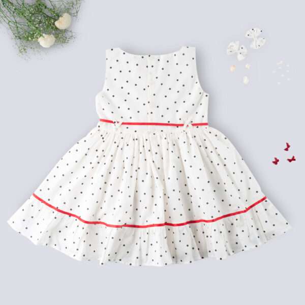 Rear image of sleeveless polka dot ivory cotton dress with red satin belt and hand embroidered bow embellishments