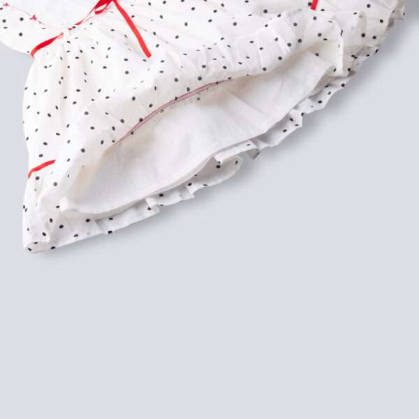 Close-up of hem of sleeveless polka dot ivory cotton dress with red satin belt and hand embroidered bow embellishments