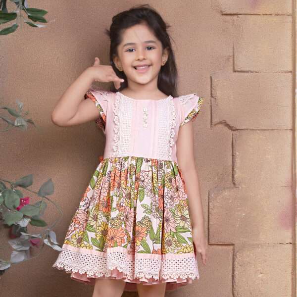 A little girl wearing floral cotton dress with a peach yoke and hem with beautiful lace trims and hand embroidery