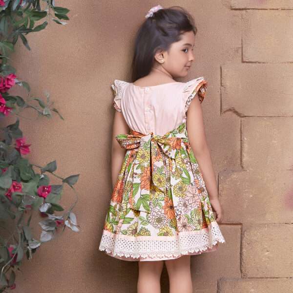 Rear image of a girl in floral cotton dress with a peach yoke and hem with beautiful lace trims and hand embroidery