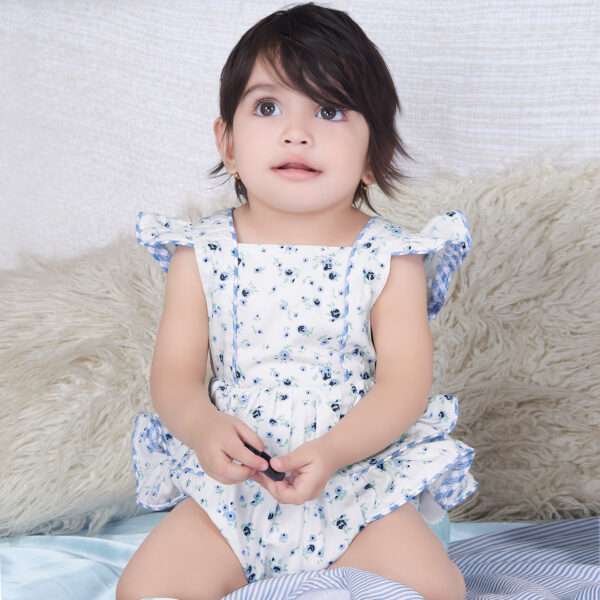 A baby girl in blue floral printed onesie with back crossover straps and ruffles on the bottom with contrast trims
