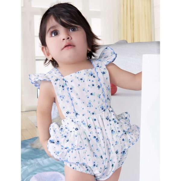 A baby girl in blue floral printed onesie with back crossover straps and ruffles on the bottom with contrast trims
