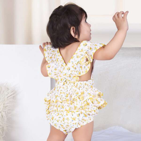 A baby girl in yellow floral printed onesie with back crossover straps and ruffles on the bottom with contrast trims