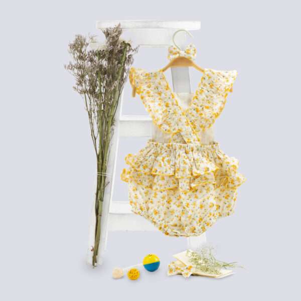 Flatlay image of yellow floral printed onesie with back crossover straps and ruffles on the bottom with contrast trims