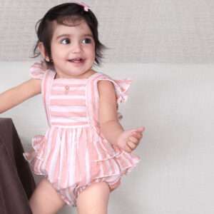 A baby girl in peach and grey striped romper with a hand embroidered flower, back crossover straps and ruffled bottom