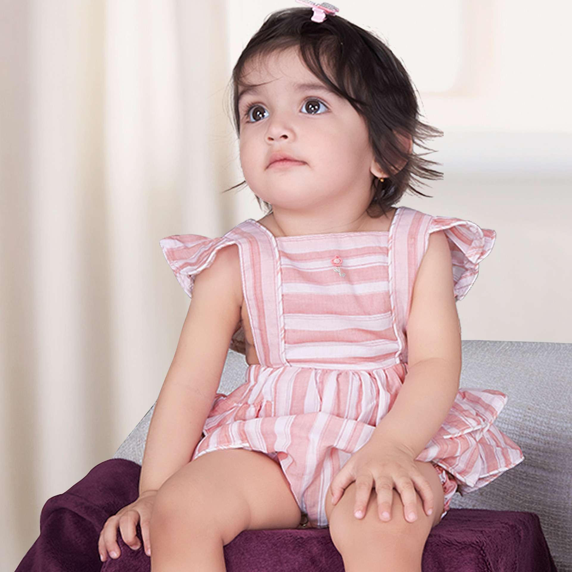A baby girl in peach and grey striped romper with a hand embroidered flower, back crossover straps and ruffled bottom