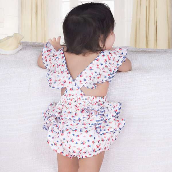 Back side of a baby girl in blue floral printed onesie with back crossover straps and ruffles on the bottom