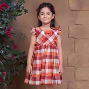 A little girl in plaid dress with shades of rust orange, flutter sleeves, side ties and decorative bow in the yoke