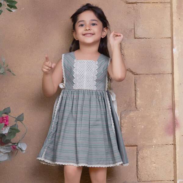 A young girl wearing striped sleeveless dress with charming side bows and delicate lace trims