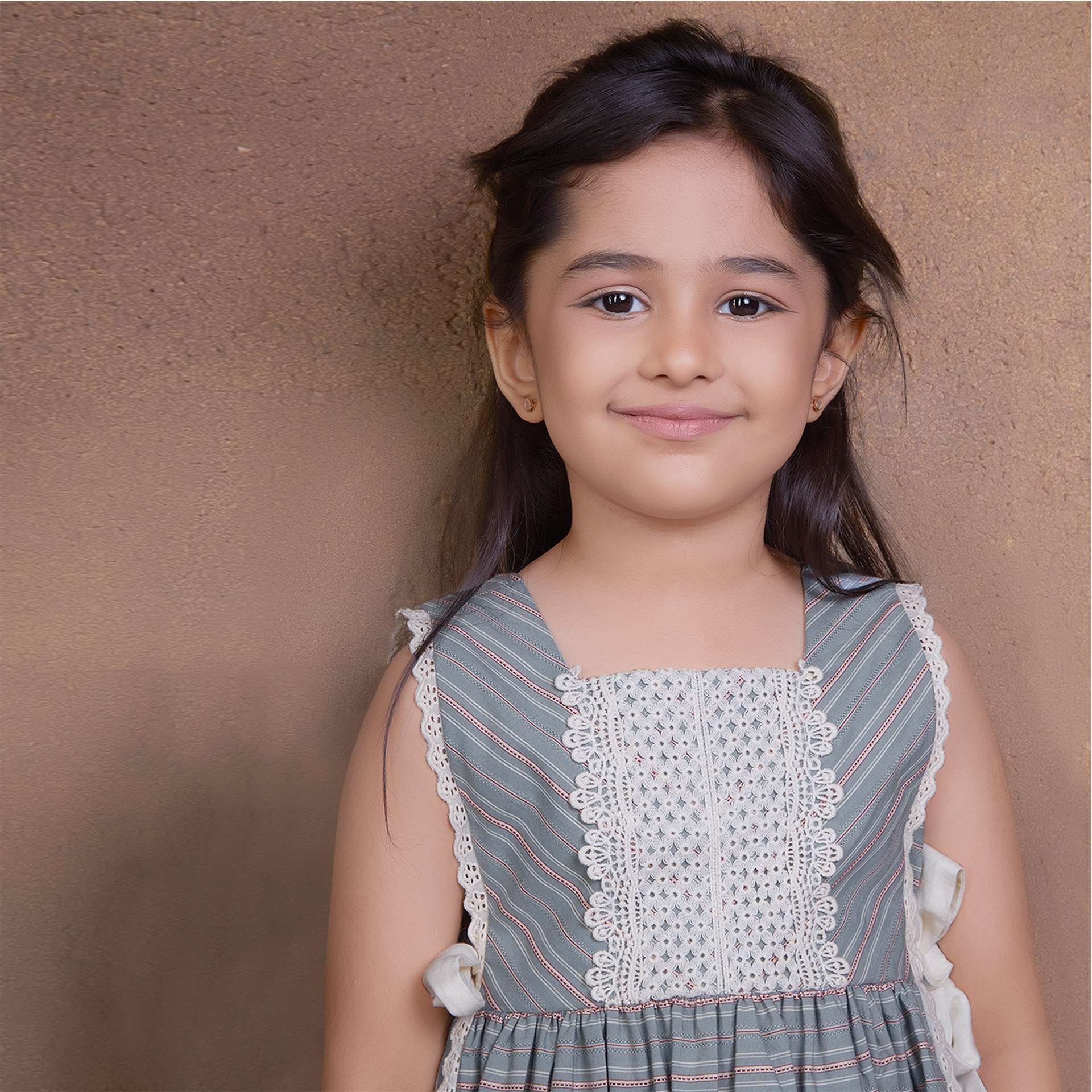 A young girl showcasing striped sleeveless dress with charming side bows and delicate lace trims