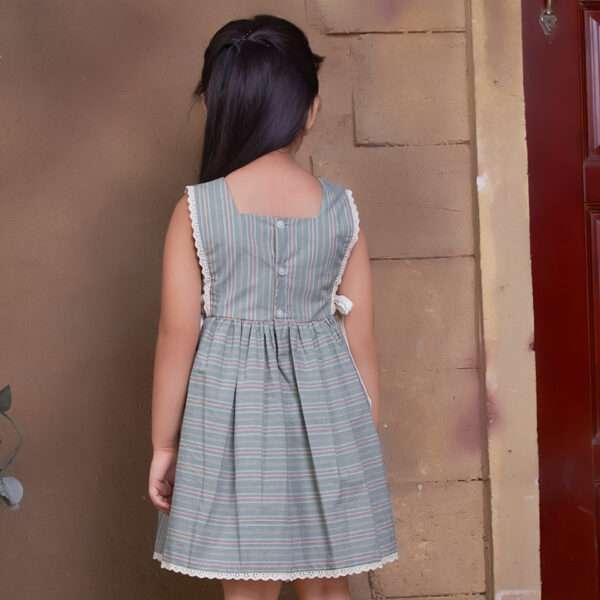 Rear image of a little girl showcasing striped sleeveless dress with charming side bows and delicate lace trims