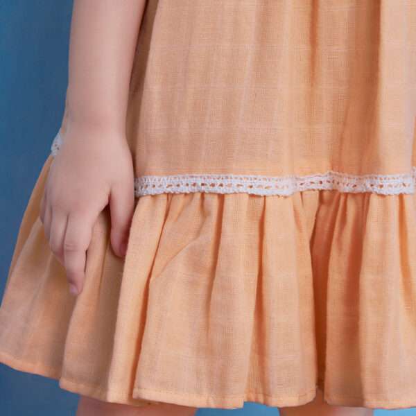 Close-up of peach gauze dress with hand-embroidered flowers in the yoke, ivory lace trims and a ruffled hem