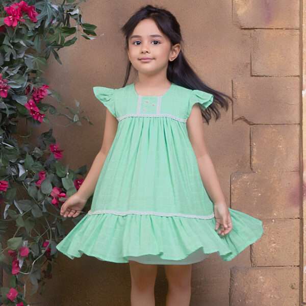 A little girl in aqua double gauze fabric dress with hand-embroidered flower details in the yoke with ivory lace trims