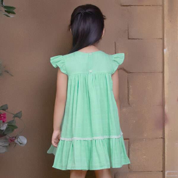Rear image of girl in aqua double gauze fabric dress with hand-embroidered flower details with ivory lace trims