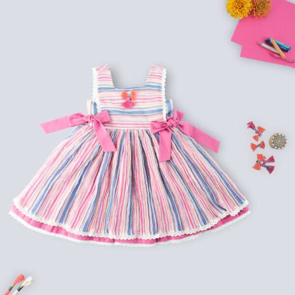 Flatlay of sleeveless multi-color stripe dress with side ties, lace trims and a decorative thread bow