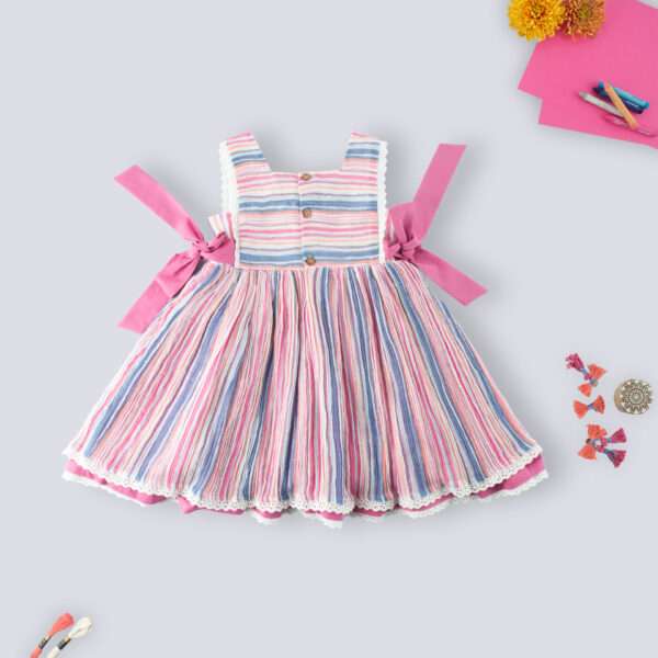 Flatlay of rear side of sleeveless multi-color stripe dress with side ties, lace trims and a decorative thread bow