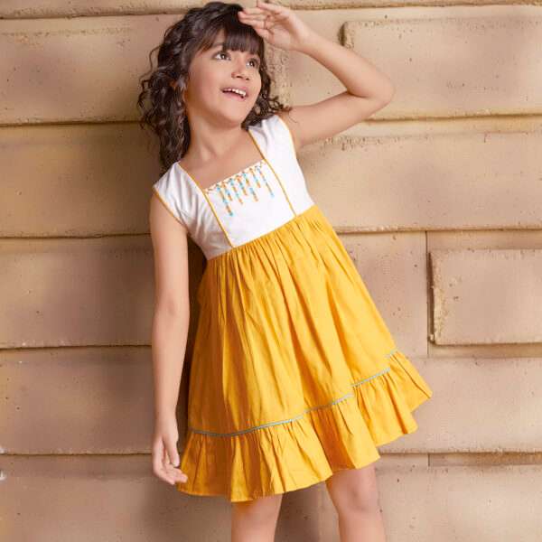 A young girl wearing sleeveless golden yellow dress with a 'Toran' hand embroidered yoke and hem ruffles