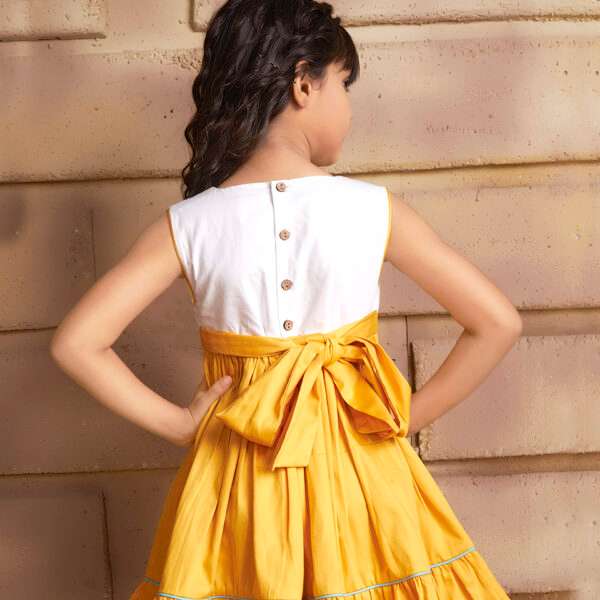 Rear image of a girl wearing sleeveless golden yellow dress with a 'Toran' hand embroidered yoke and hem ruffles