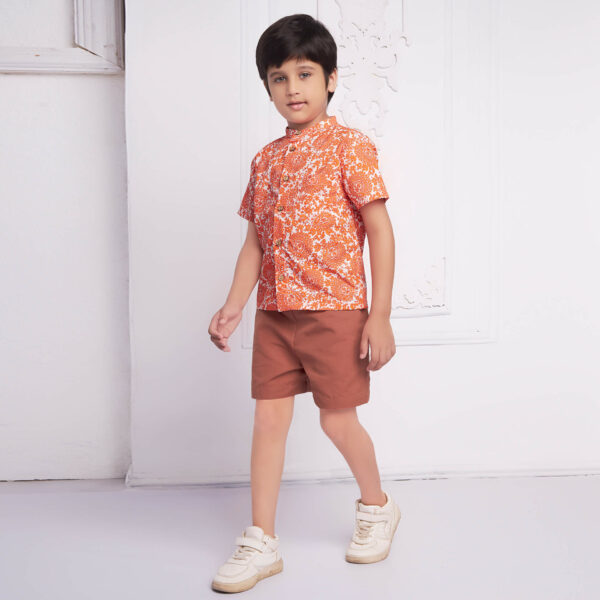 Boy wallking wearing a shirt and shorts set in tones of rust to orange