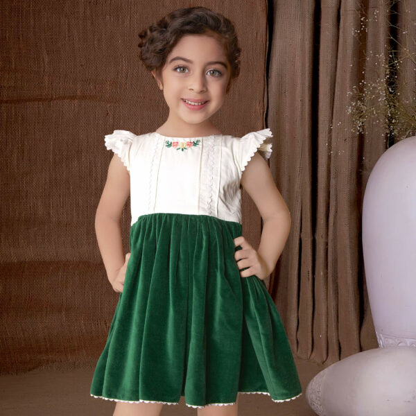 With hands on hips, a little girl stands in a green velvet dress adorned with ivory lace