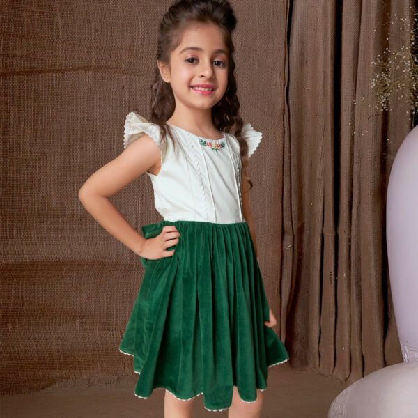 Side pose of a girl wearing a green velvet embroidered dress with an attached embellished bow at the waist and ric rac trims