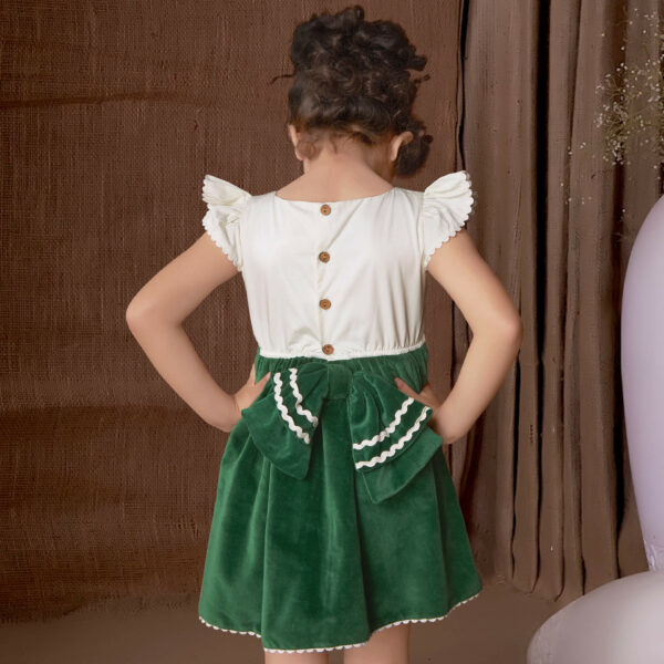 Back pose of a girl wearing a green velvet embroidered dress with an attached embellished bow at the waist and ric rac trims