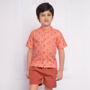 A boy wearing a peach printed mandarin collared shirt paired with rust shorts.