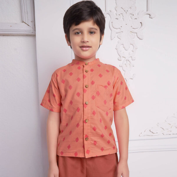 Boy wears a peach and pink print shirt with wood buttons