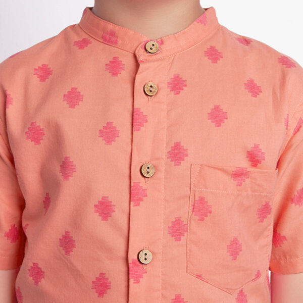 Detailed close-up of a peach printed boys shirt fastened by wood buttons, featuring pocket details