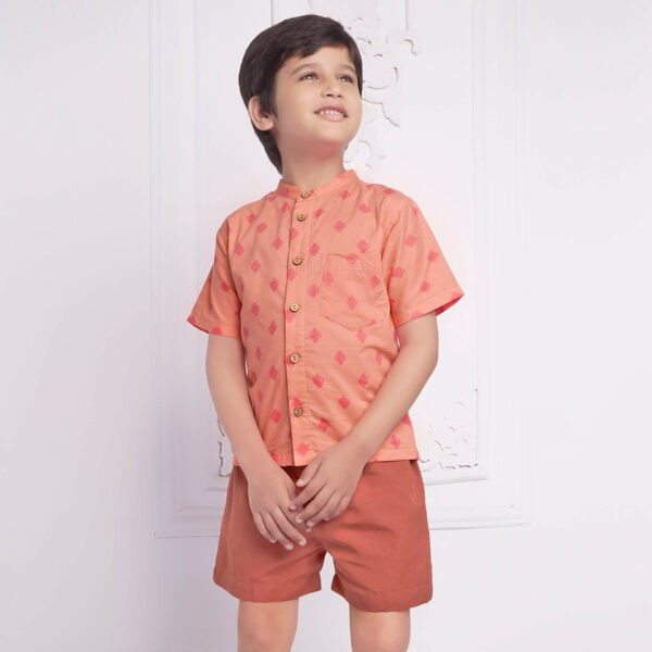Smiling boy wearing a peach print shirt and rust shorts