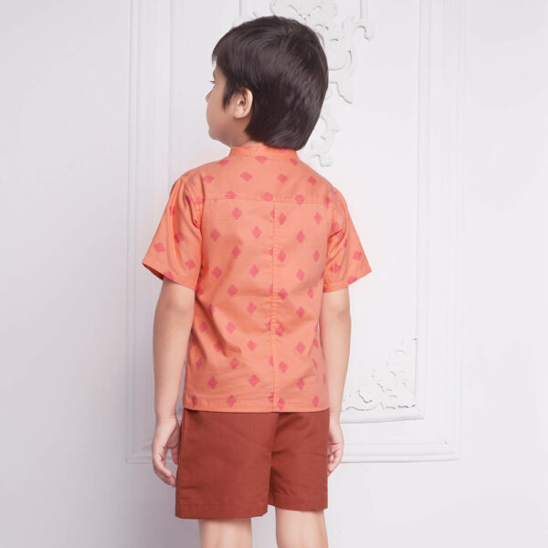 Back view of a boy wears peach printed shirt matched with rust shorts, both with pockets.