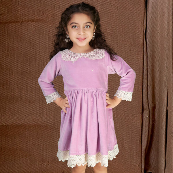 With hands on hips, a little girl stands in a purple velvet dress adorned with white lace