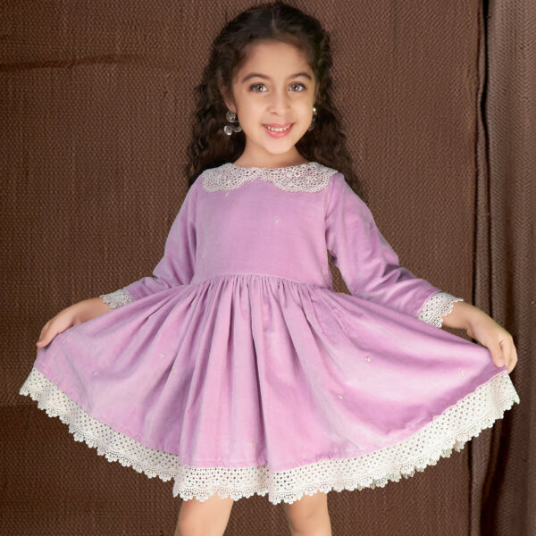 Posing in a lavender velvet dress, the girl playfully stretches the skirt with both hands