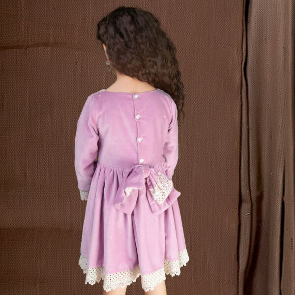 Back view of a girl wearing a lavender velvet dress with an attached embellished bow at the waist