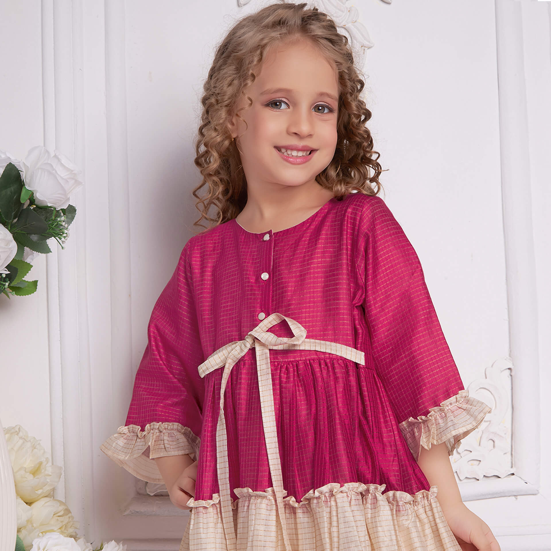 With a slight turn, a girl posing in pink and ivory chanderi dress with front tie up sash