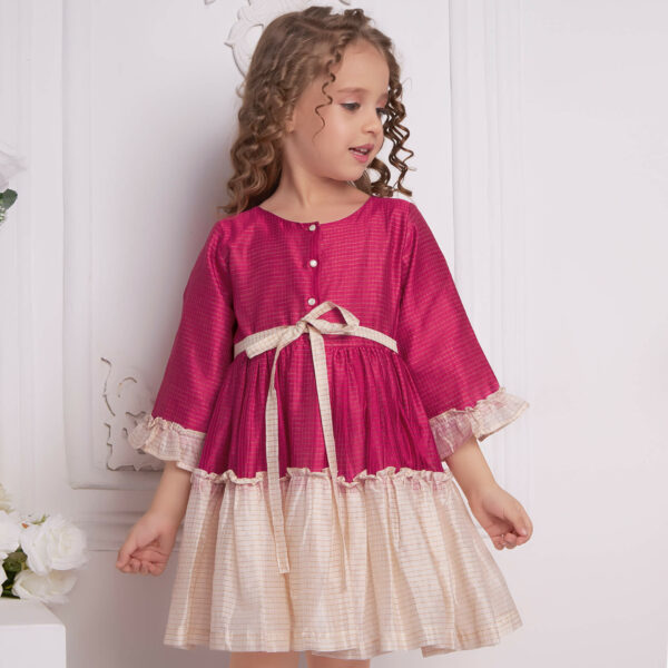 A pink and ivory chanderi ruffle dress showcased by a young girl, with front pearl buttons and a tie-up sash