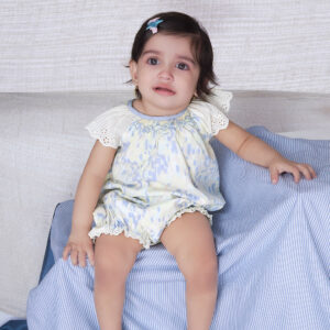 A baby seated wearing watercolor printed smocked onesie adorned with lace