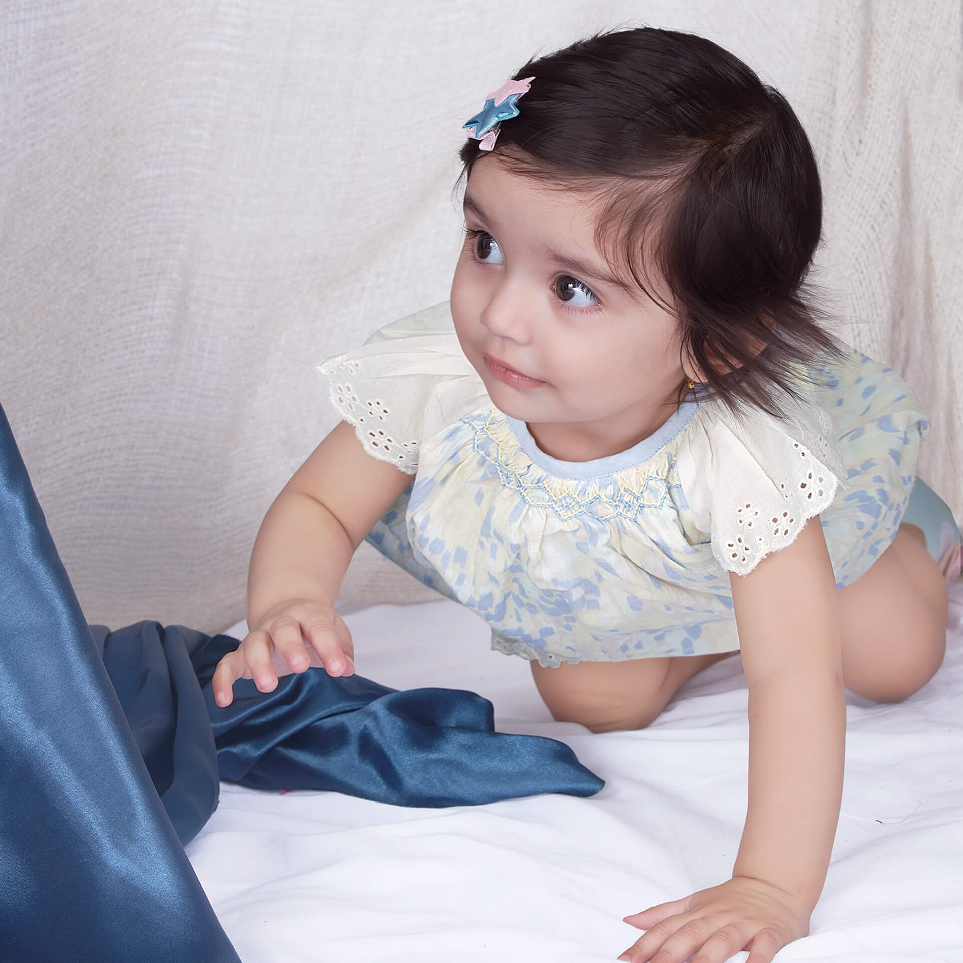 A baby girl crawls in a watercolor smocked onesie with lace trims