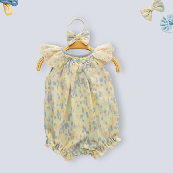 Flat lay of a water color smocked onesie for baby girls, with delicate lace
