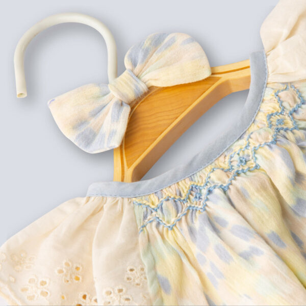 Flat lay of a close-up view of a watercolor smocked onesie for a baby girl on a hanger