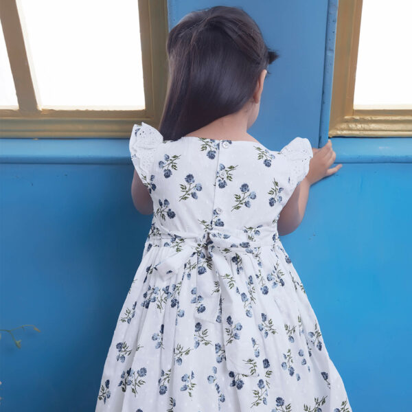Back view of a girl in a white swiss dot floral printed smock dress