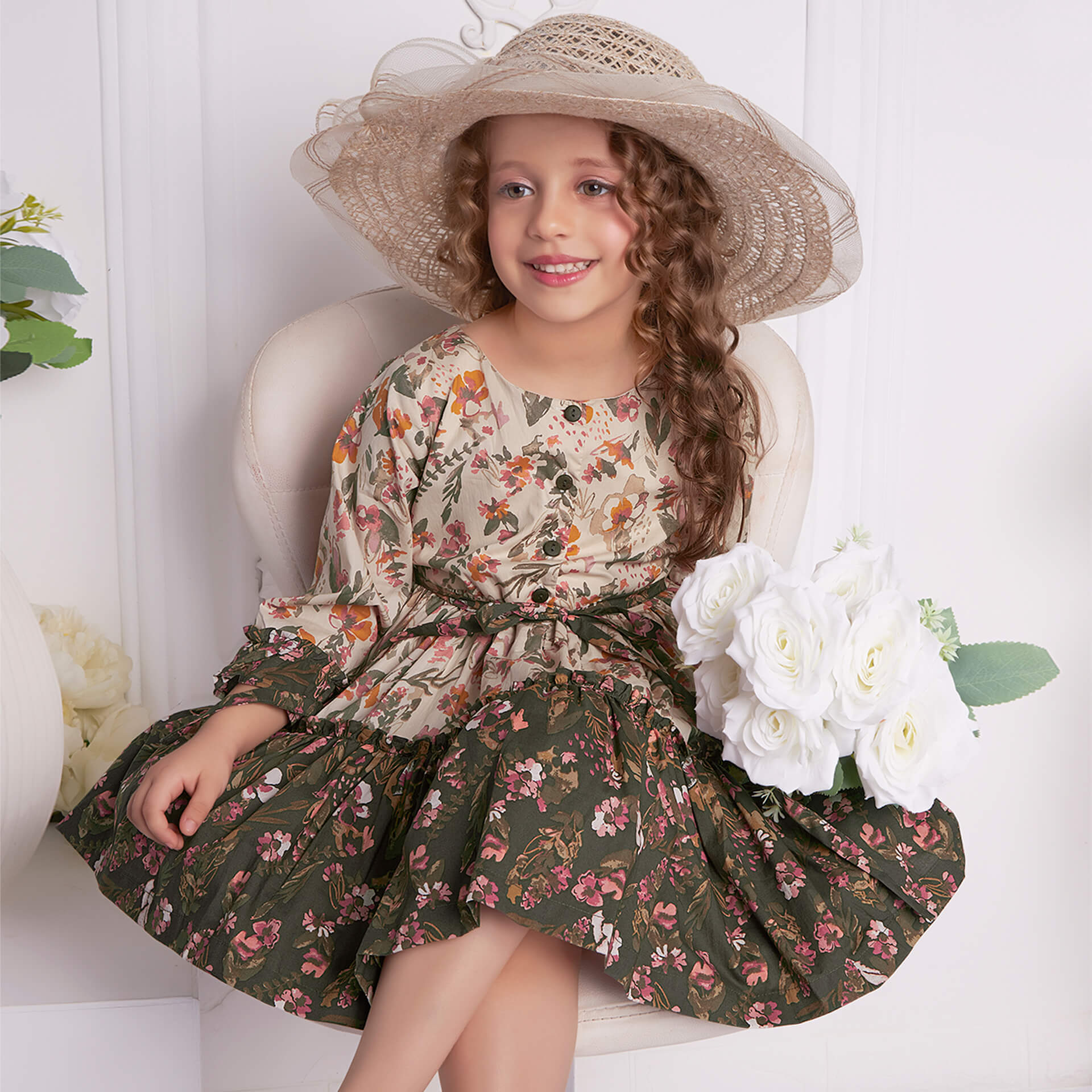 Hat-topped, a little girl seated wearing cream and green floral printed ruffle dress